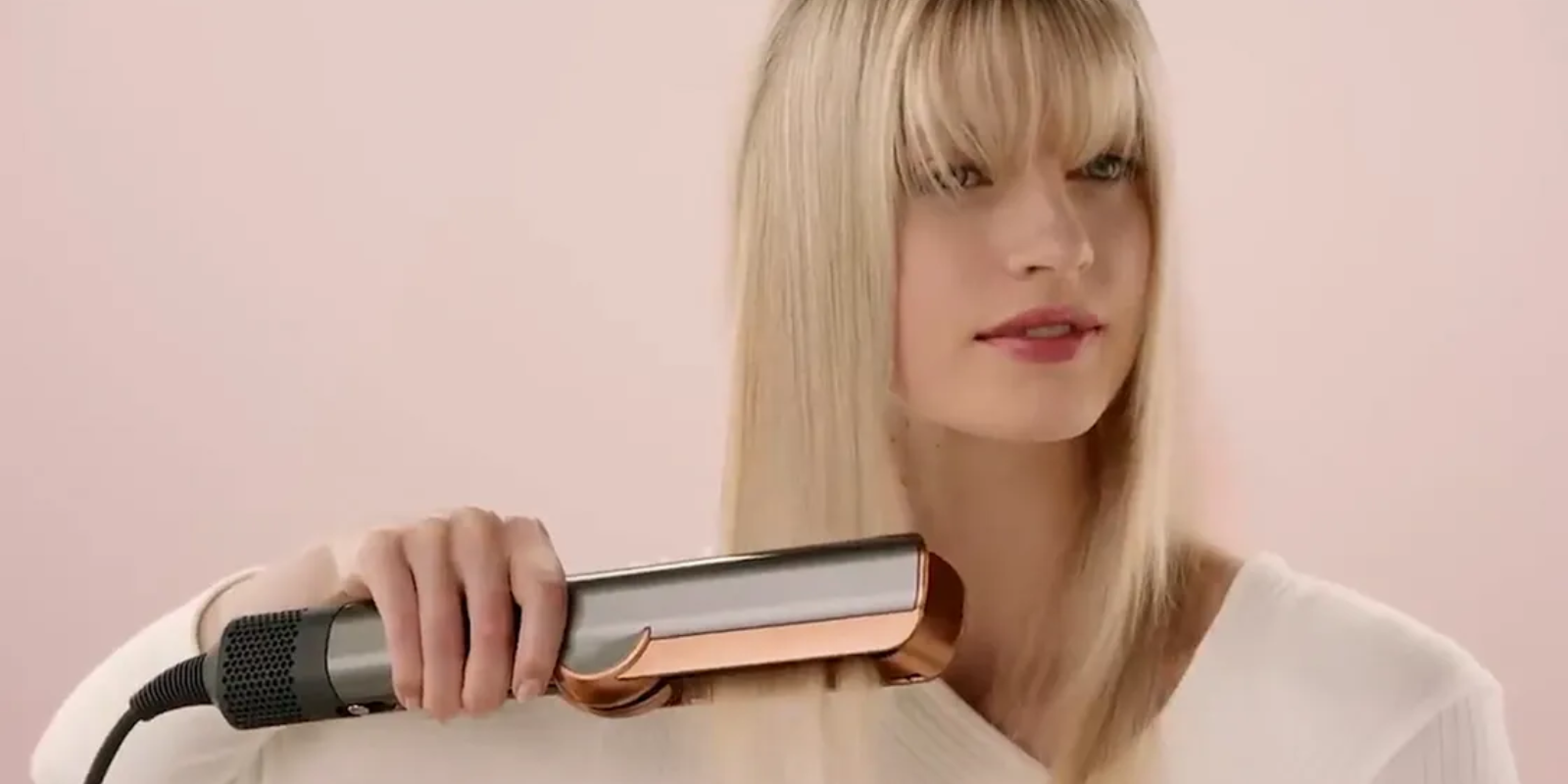 Woman holding a dyson airstrait against a pink background